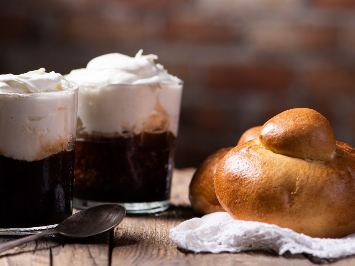 Kaffee-Granita in zwei Gläsern mit Schlagsahne, daneben ein brioche col tuppo.