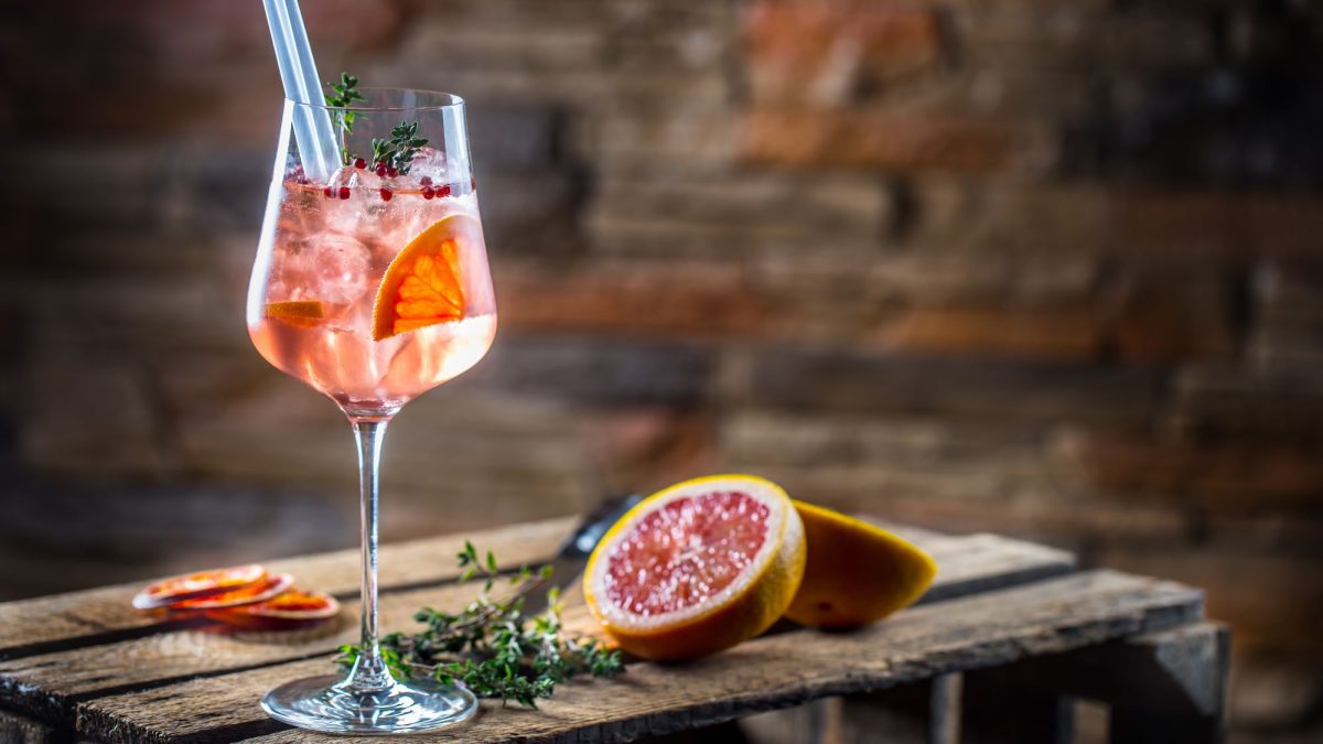 Ein Glas Lillet Jolie mit Grapefruitscheiben, rosa Pfeffer und Eiswürfeln in einem Glas.