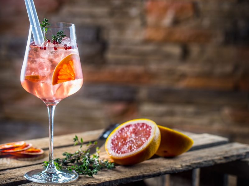 Ein Glas Lillet Jolie mit Grapefruitscheiben, rosa Pfeffer und Eiswürfeln in einem Glas.