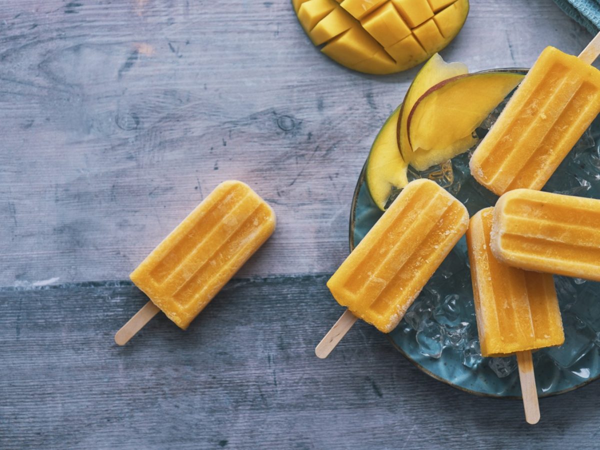 Mango-Lassi-Eis auf einem blauen Teller auf grauem Hintergrund. Oben auf dem Foto eine halbe Mango