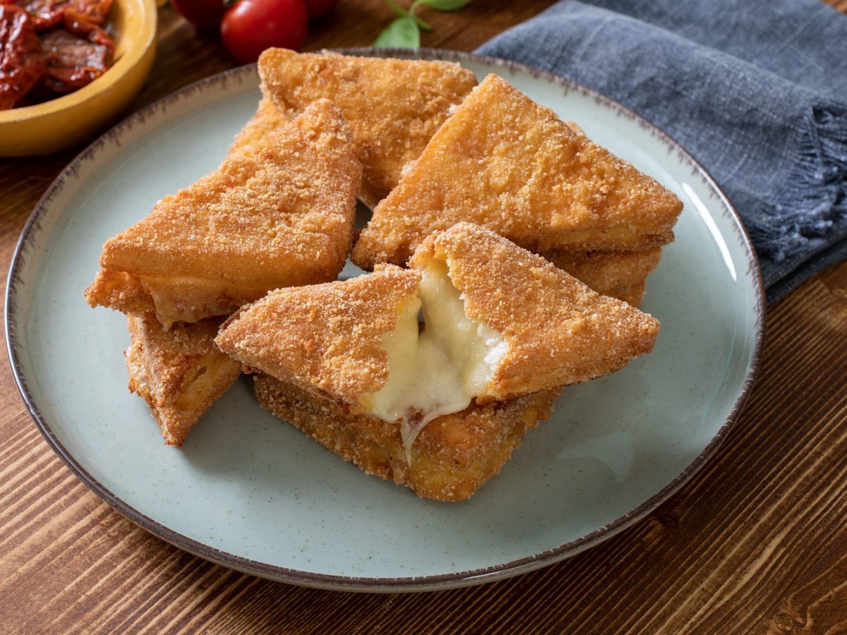 Mozzarella in carrozza auf einem blauen Teller vor einem hölzernen Untergrund.