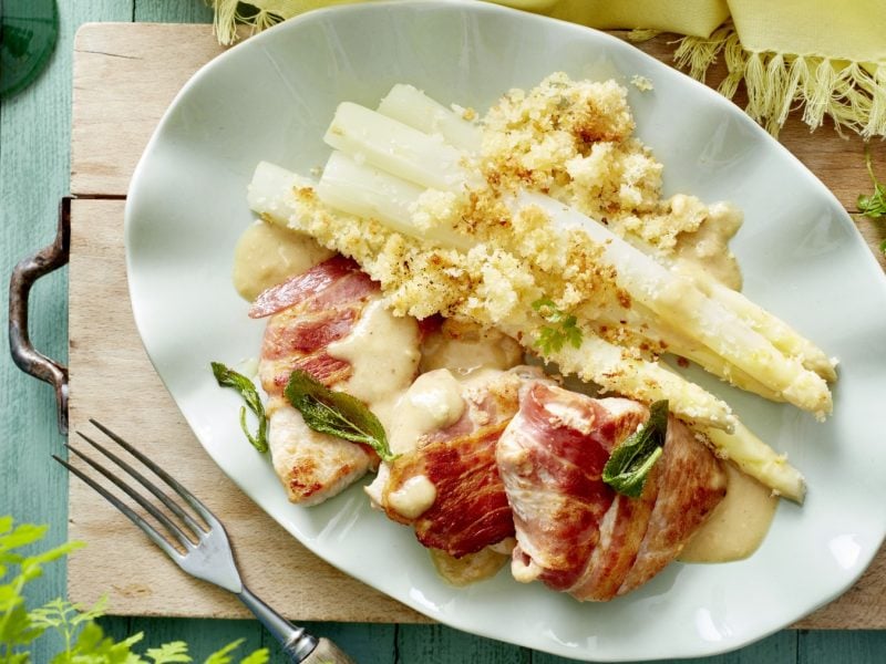 Ofen-Spargel mit Speck-Schnitzel auf weißem Teller mit Holzuntergrund.