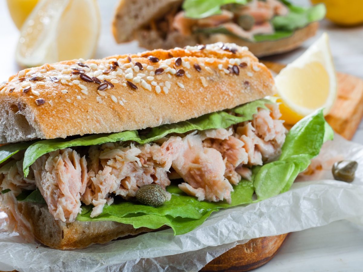 Ein Baguette mit Thunfischsalat belegt auf weißem Pergamentpapier. Alles von der Seite fotografiert.