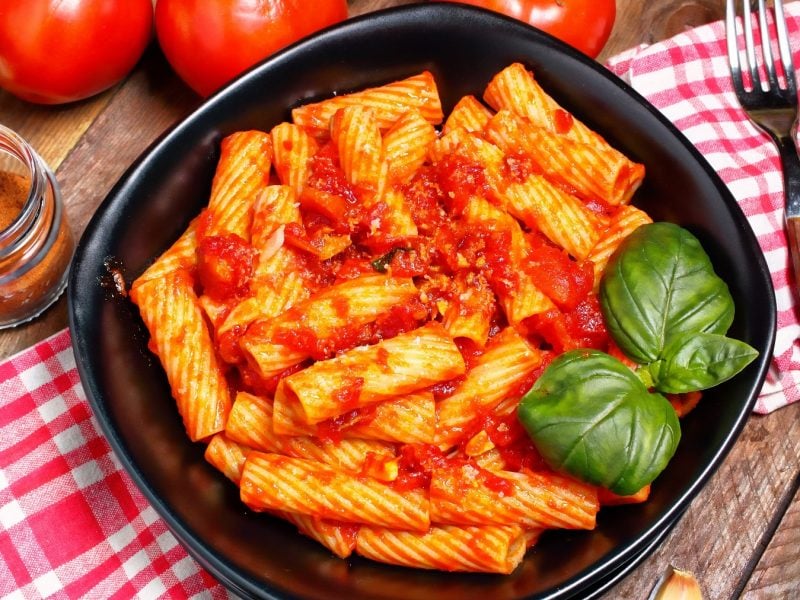 Totiglioni mit Tomatensauce mit Thunfisch mit Basilikumblättern auf einem schwarzen Teller auf einer karierten Tischdecke.