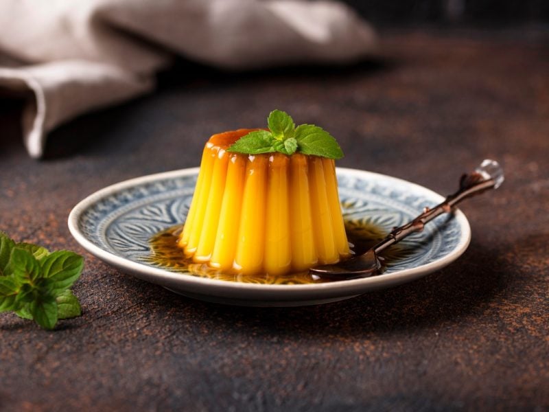 Veganer Flan auf einem weiß/blauen Teller auf braunen Hintergrund.