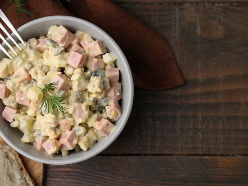 Ein Schälchen mit böhmischen Kartoffelsalat, garniert mit Dill, daneben zwei Scheiben knuspriges Weißbrot auf einem Holztisch.