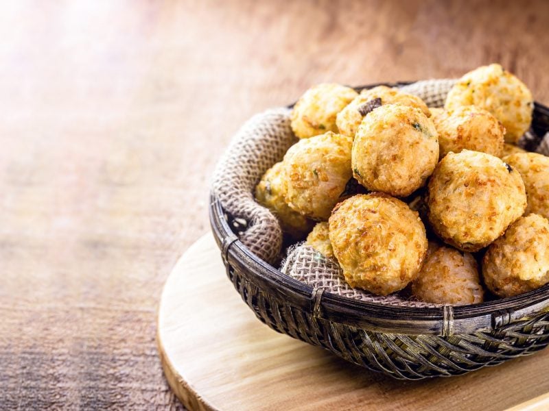 Bolinhos de arroz in einer dunklen Schüssel vor einem hellen, ausgeleuchteten Hintergrund.