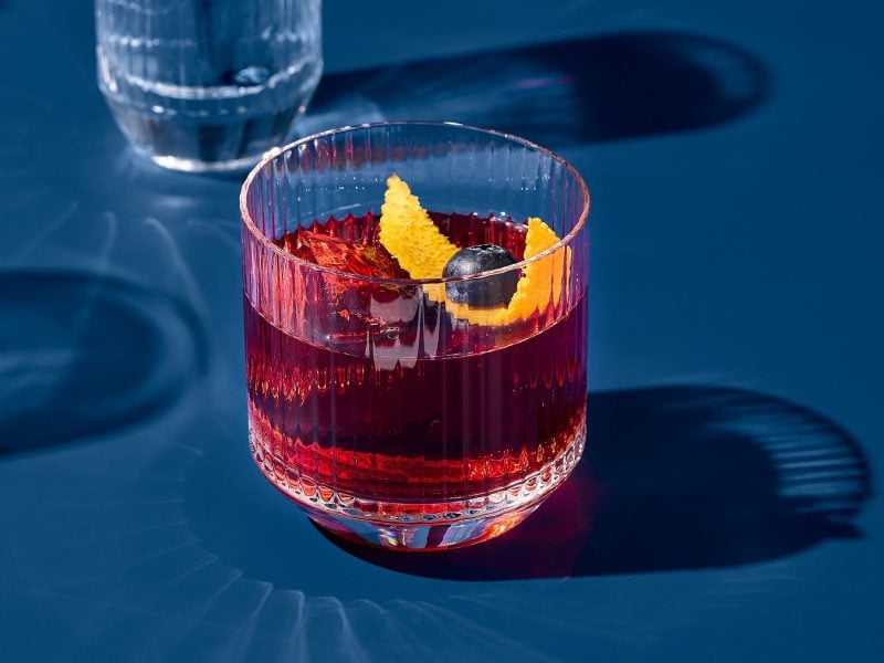 Ein Glas mit dem Campari Amalfi auf blauem Untergrund direkt in der Sonne fotografiert.