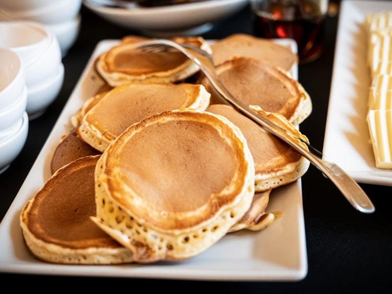 Draufsicht, schräg: eine weiße Platte mit Buchweizen-Quark-Pancakes. Daneben liegen edle weiße leere Schalen. soowie dünne scheiben Knäckebrot.