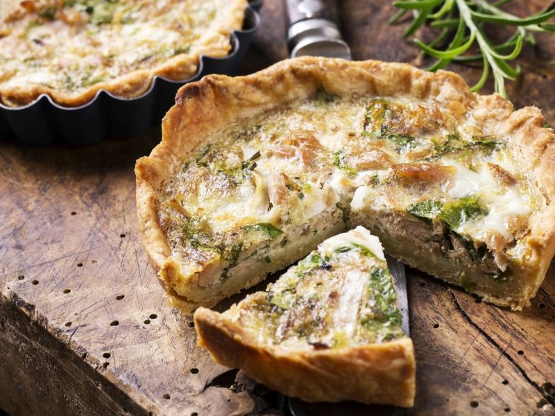 Draufsicht: Zwei Mini-Quiche mit Thunfisch liegen auf einem rustikalen Untergrund aus Holz. Daneben liegt in Rosmarinzweig.