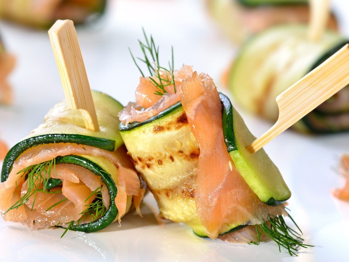 Frontalsicht: Zucchini-Lachs-Röllchen auf einem weißen Untergrund.