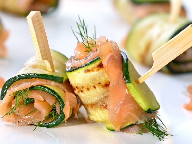 Frontalsicht: Zucchini-Lachs-Röllchen auf einem weißen Untergrund.