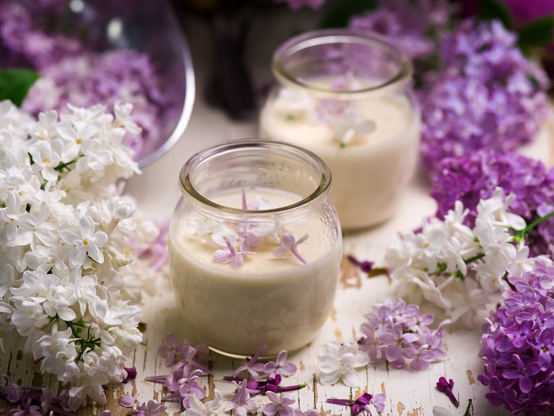 Zwei Flieder-Honig-Possets im Glas neben Fliederdolden.