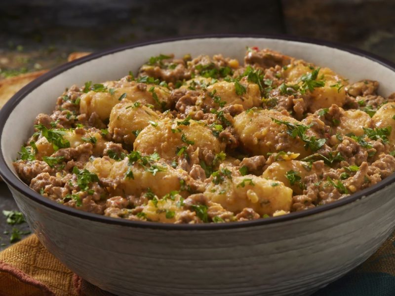 Schüssel mit cremiger Gnocchi-Hackfleisch-Pfanne, garniert mit frischer Petersilie, im Vordergrund ein Stück Brot