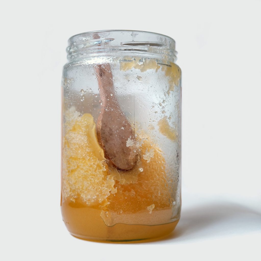 Ein Glas mit kristallisiertem Honig vor grauem Hintergrund.