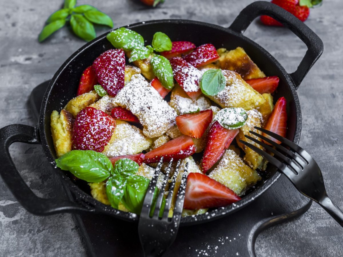 Kaiserschmarrn mit Erdbeeren in einer schwarzen Pfanne auf grauem Hintergrund.