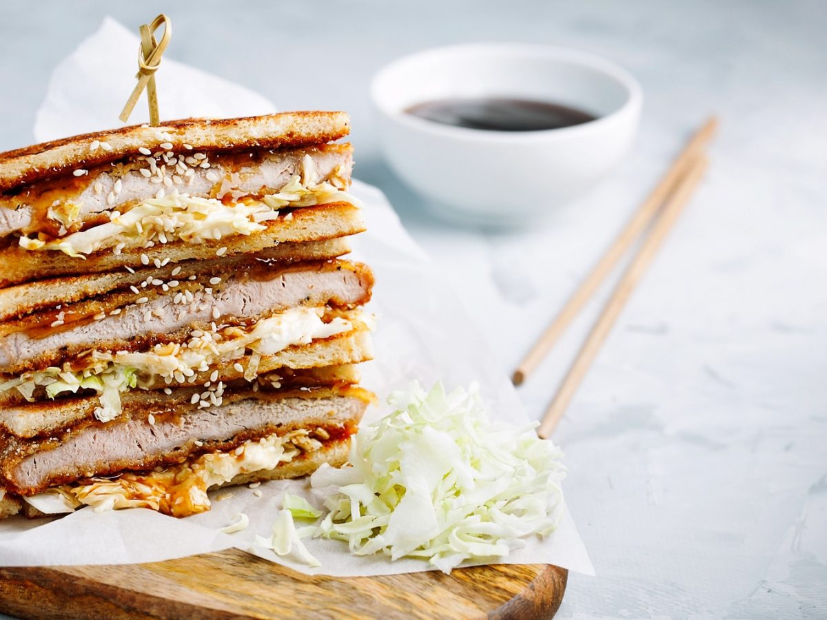 Das angeschnittene Sandwich auf einem Holzbrett und hellem Unter- und Hintergrund. Nah und von der Seite fotografiert.