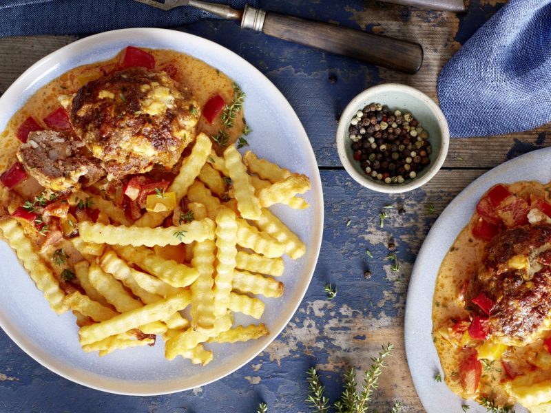 Zwei Teller Mini-Braten in Paprika-Rahm auf hölzernem Hintergrund. In der Mitte ein Schälchen mit Pfefferkörnern und darunter Thymian verteilt.