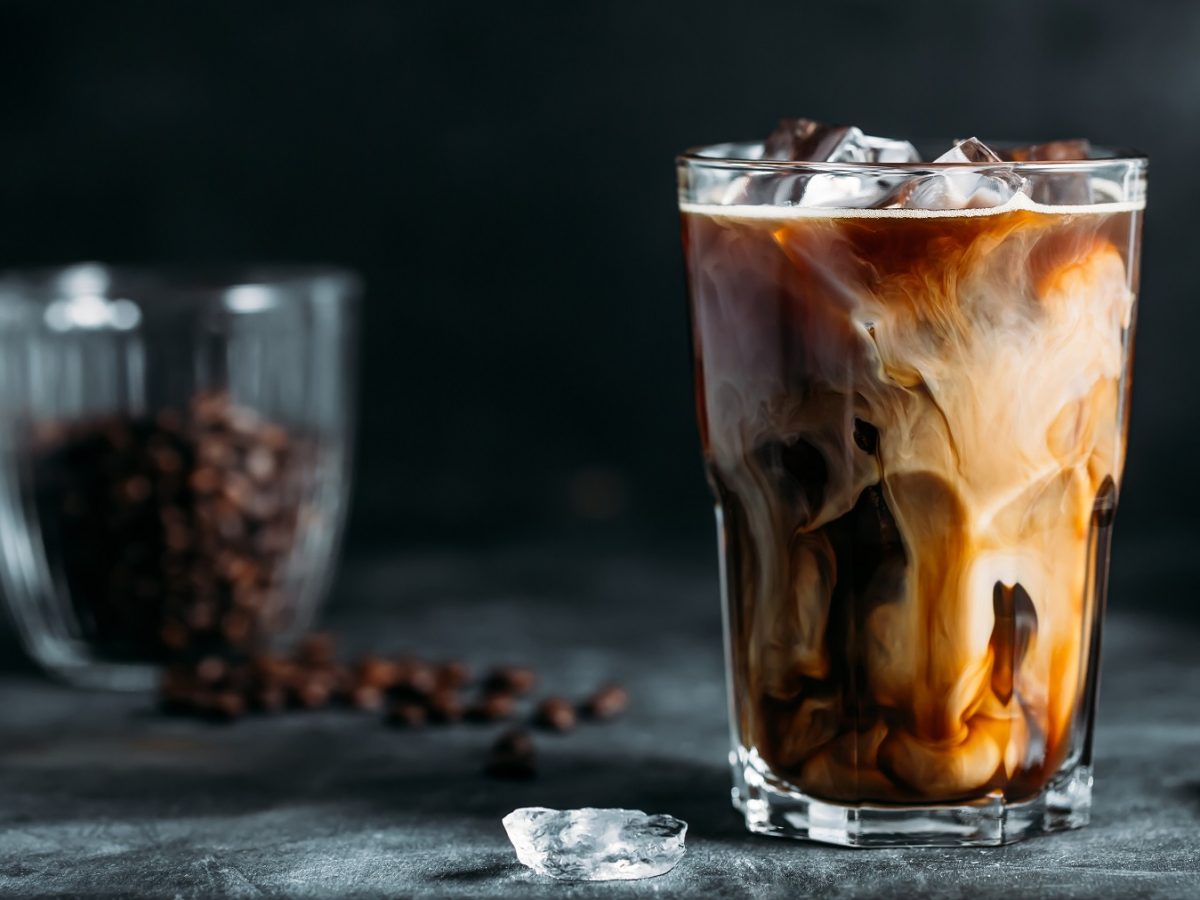 Proffee in einem Glas vor dunklem Hintergrund, wo ein Glas mit Kaffeebohnen steht.