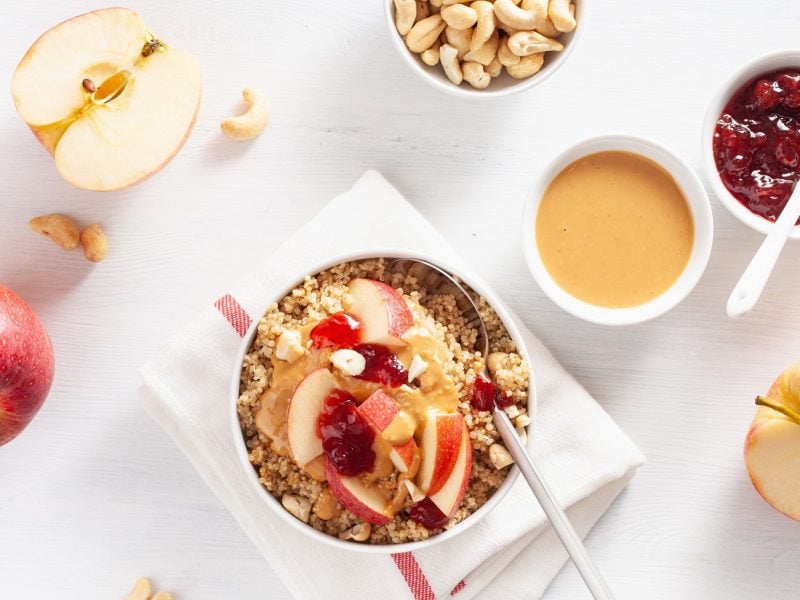 Quinoa Porridge von oben daneben, halbierter Apfel, Schale mit Erdnussmus und Marmelade.