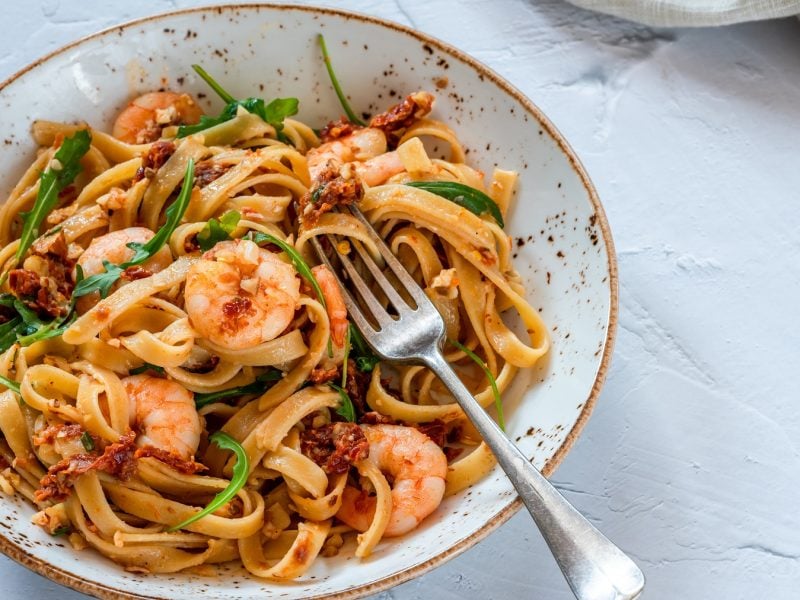 Ein heller, tiefer Teller mit der Pasta auf einem grauen Steintisch und einer Gabel. Alles von leicht schräg oben fotografiert.