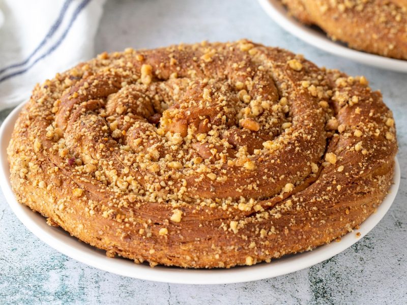 Goldbraune, knusprige Tahinli çörek auf einem weißen Teller, daneben ein weißes Leinentuch auf hellem Hintergrund.