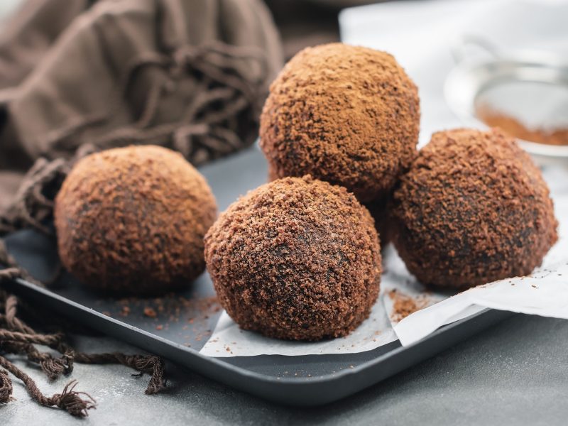 Ein grauer Teller mit einigen Tiramisu-Balls auf grauem Untergrund und mit einer braunen Tischdecke.