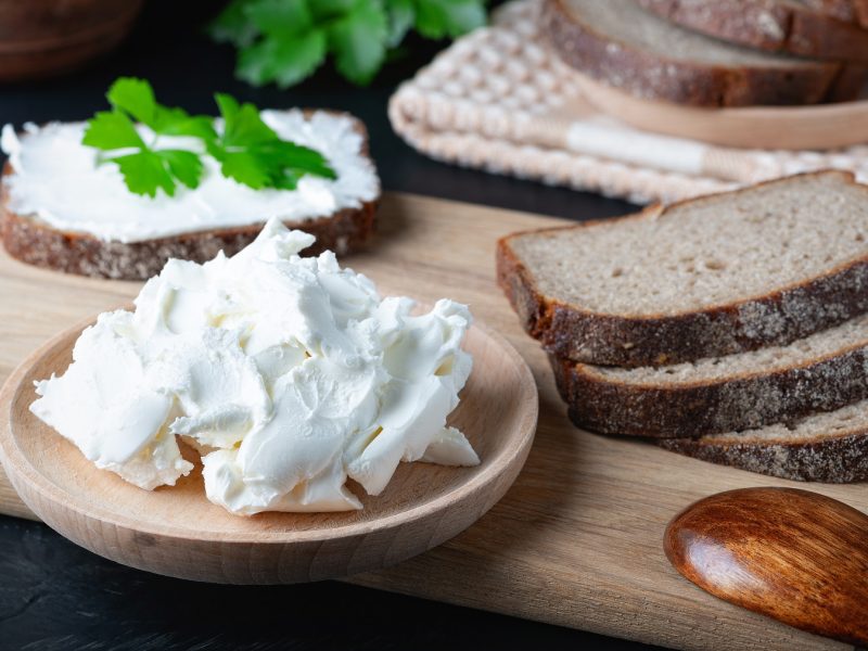 Veganer Quark auf einem Schälchen neben Brotscheiben auf einem Holzbrett.