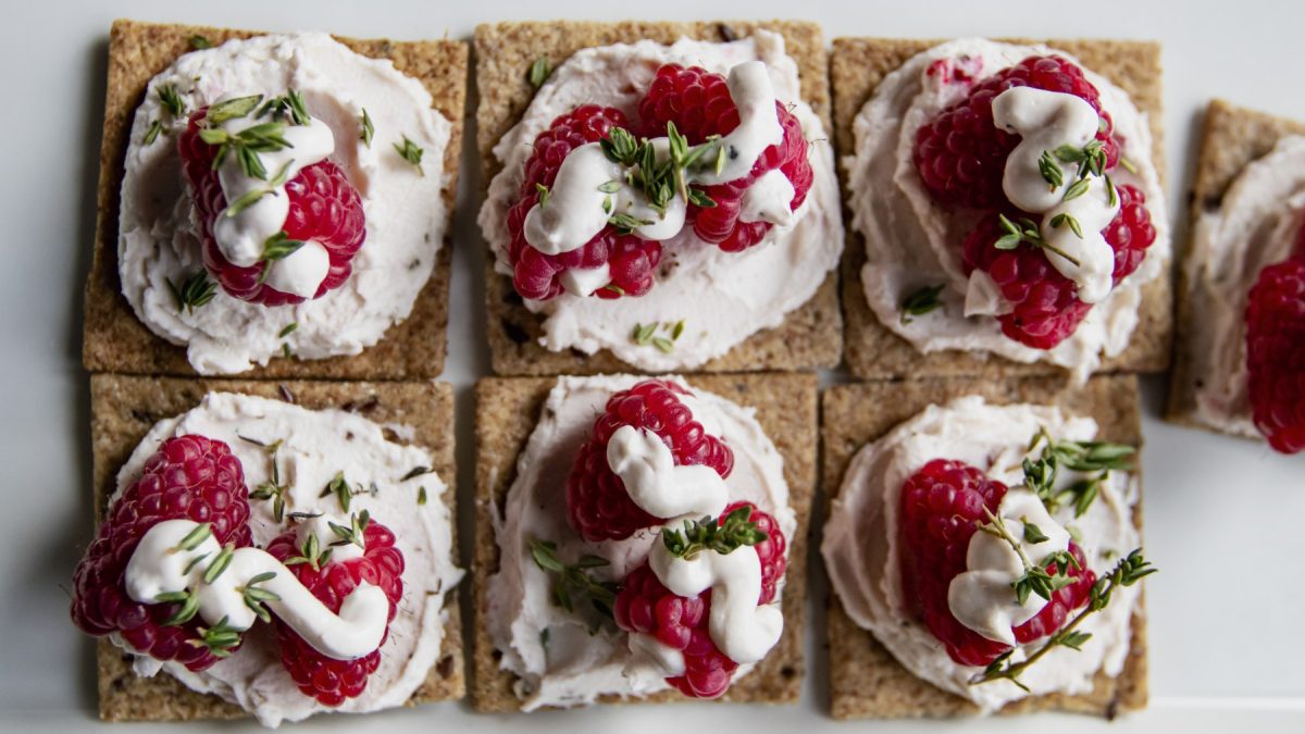 Beerige Cracker mit Ricotta auf einem hölzernen Brett auf weißem Hintergrund.