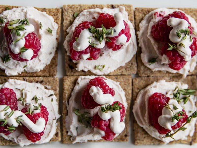 Beerige Cracker mit Ricotta auf einem hölzernen Brett auf weißem Hintergrund.