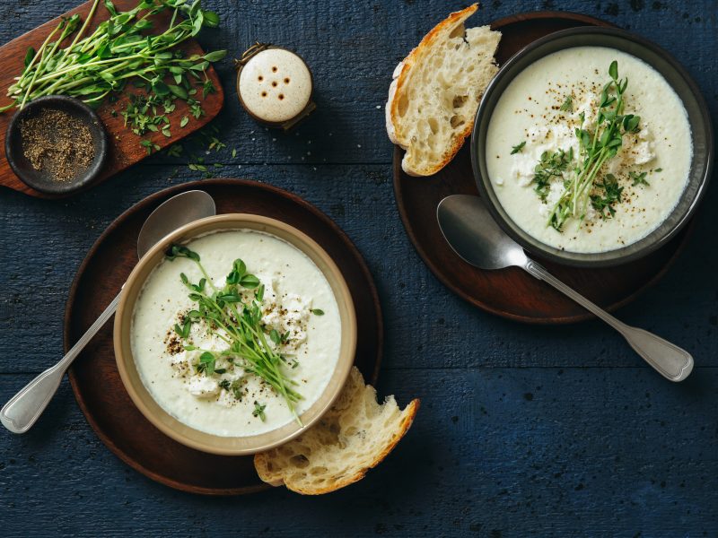 Blumenkohlsuppe mit Feta und Microgreens in zwei Schüssel und Brotscheiben von oben fotografiert.