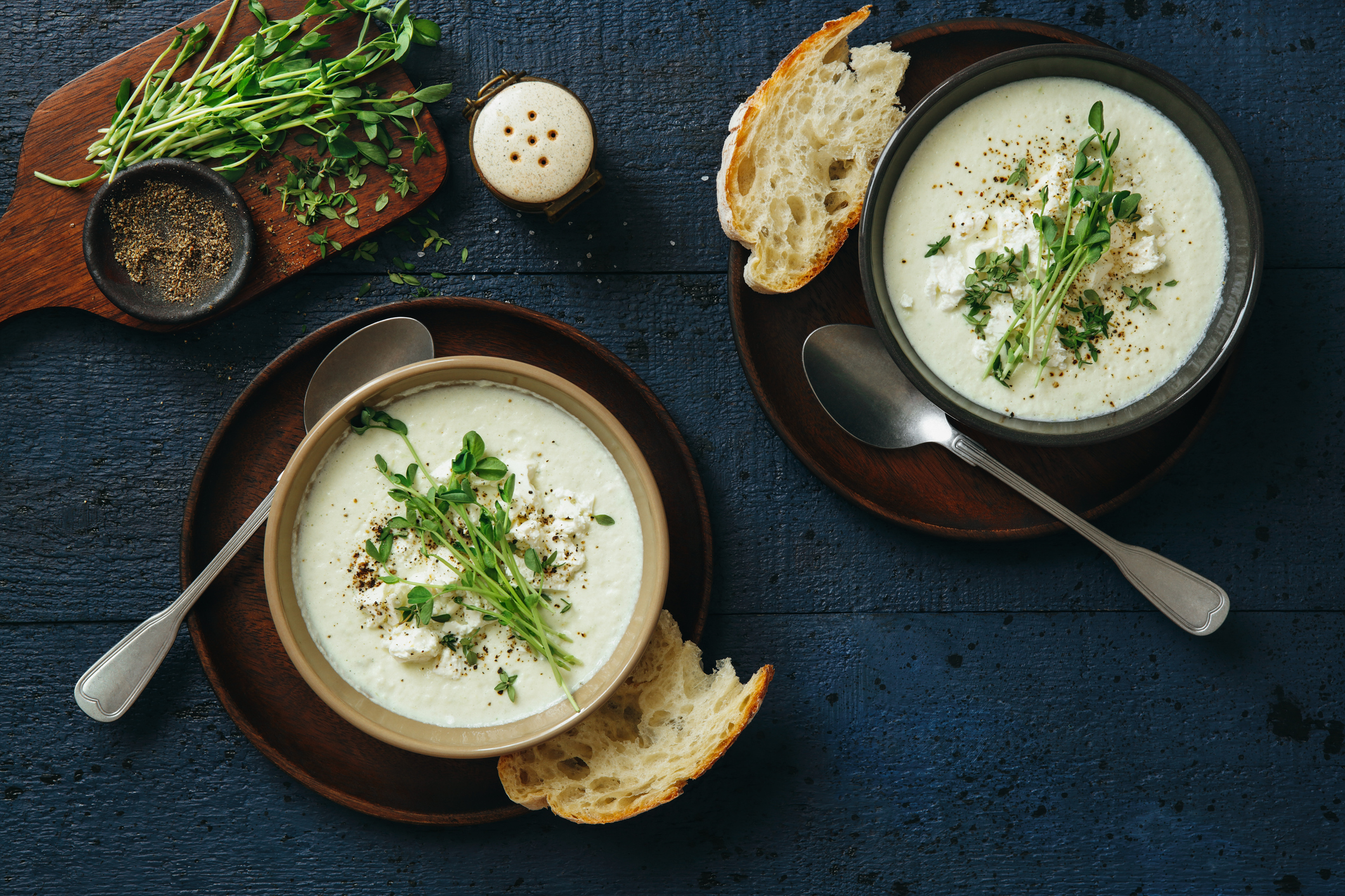 Blumenkohlsuppe mit Feta und Microgreens in zwei Schüssel und Brotscheiben von oben fotografiert.