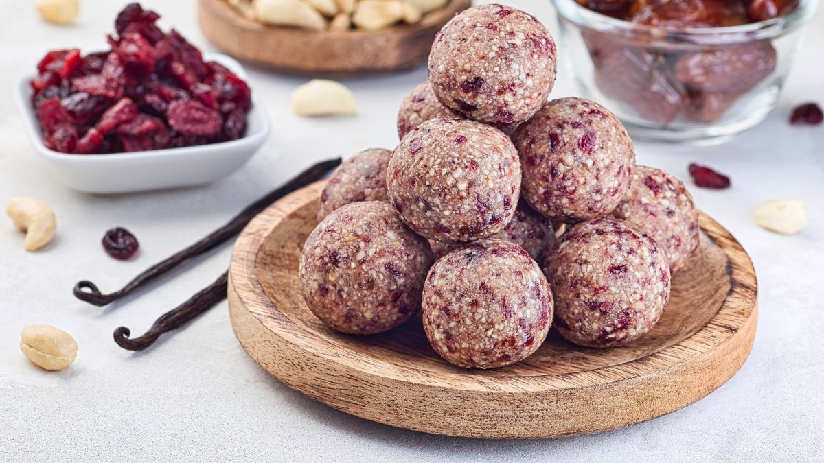 Cranberry-Energyballs auf einem Holzteller. Im Hintergrund die Zutaten für die Bällchen.