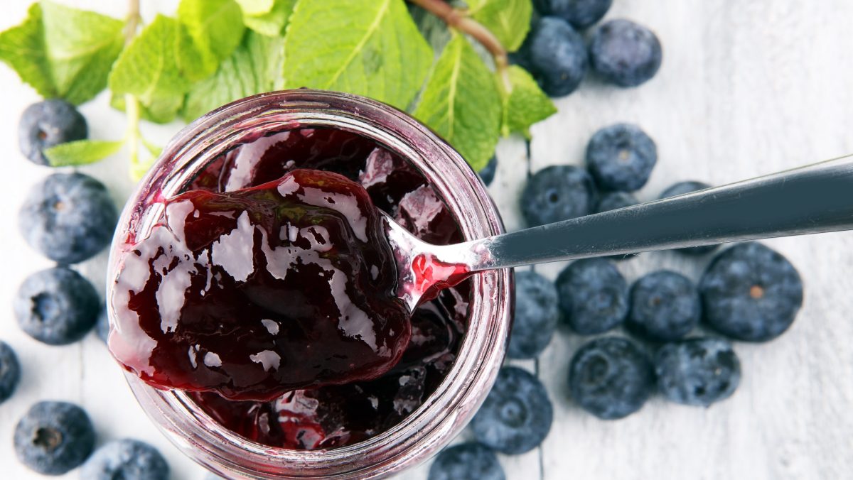 Draufsicht: Omas blaubeer-marmelade nut Vanille auf einem weißen Untergrund. Drum herum liegen frische Heidelbeeren.