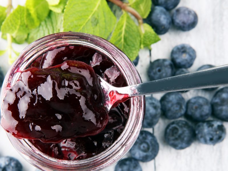 Draufsicht: Omas blaubeer-marmelade nut Vanille auf einem weißen Untergrund. Drum herum liegen frische Heidelbeeren.