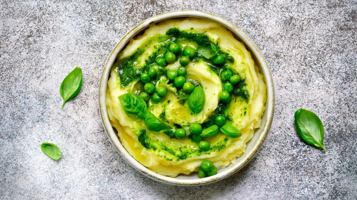 Draufsicht: Ein mediterranes Kartoffelpüree mit Pesto in einer weißen Schüssel auf grauem Untergrund.