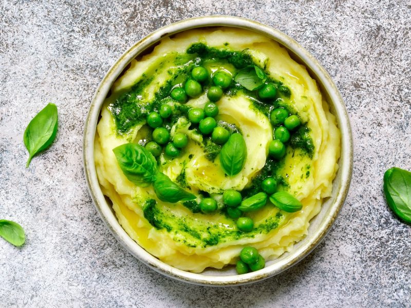 Draufsicht: Ein mediterranes Kartoffelpüree mit Pesto in einer weißen Schüssel auf grauem Untergrund.