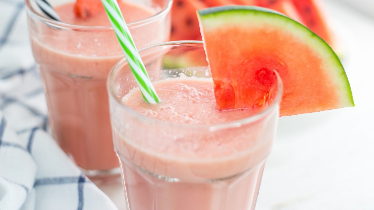 Frontal: Zwei Gläser mit einem Wassermelonen-Smoothie mit je einem Strohhalm. Die Gläser sind mit einem Scheibe Wassermelone dekoriert.