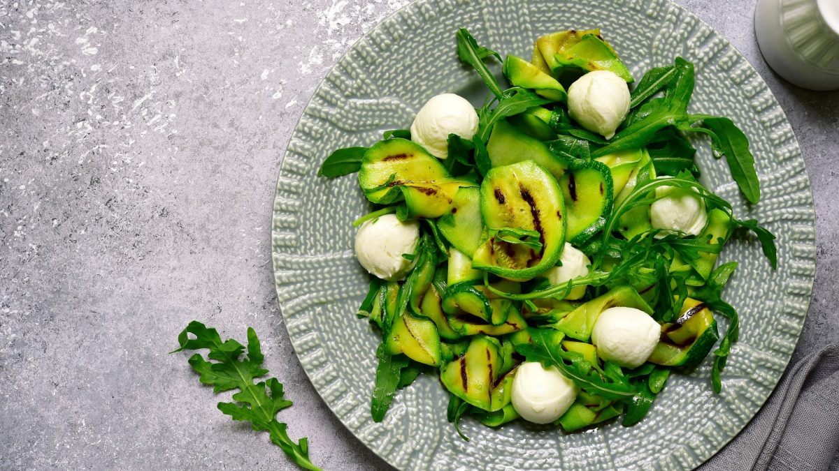 Draufsicht: Ein italienische gemusteter Teller mit einem Gegrillter Zucchini-Salat mit Mozzarella und Rucola.