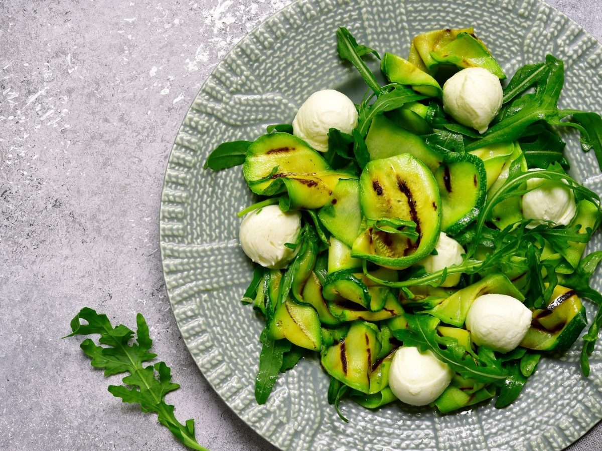 Draufsicht: Ein italienische gemusteter Teller mit einem Gegrillter Zucchini-Salat mit Mozzarella und Rucola.