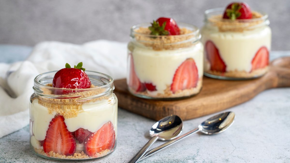 Drei Gläser mit dem Dessert auf einem grauen Tisch mit kleinem Holzbrett. Alles von der Seite fotografiert.