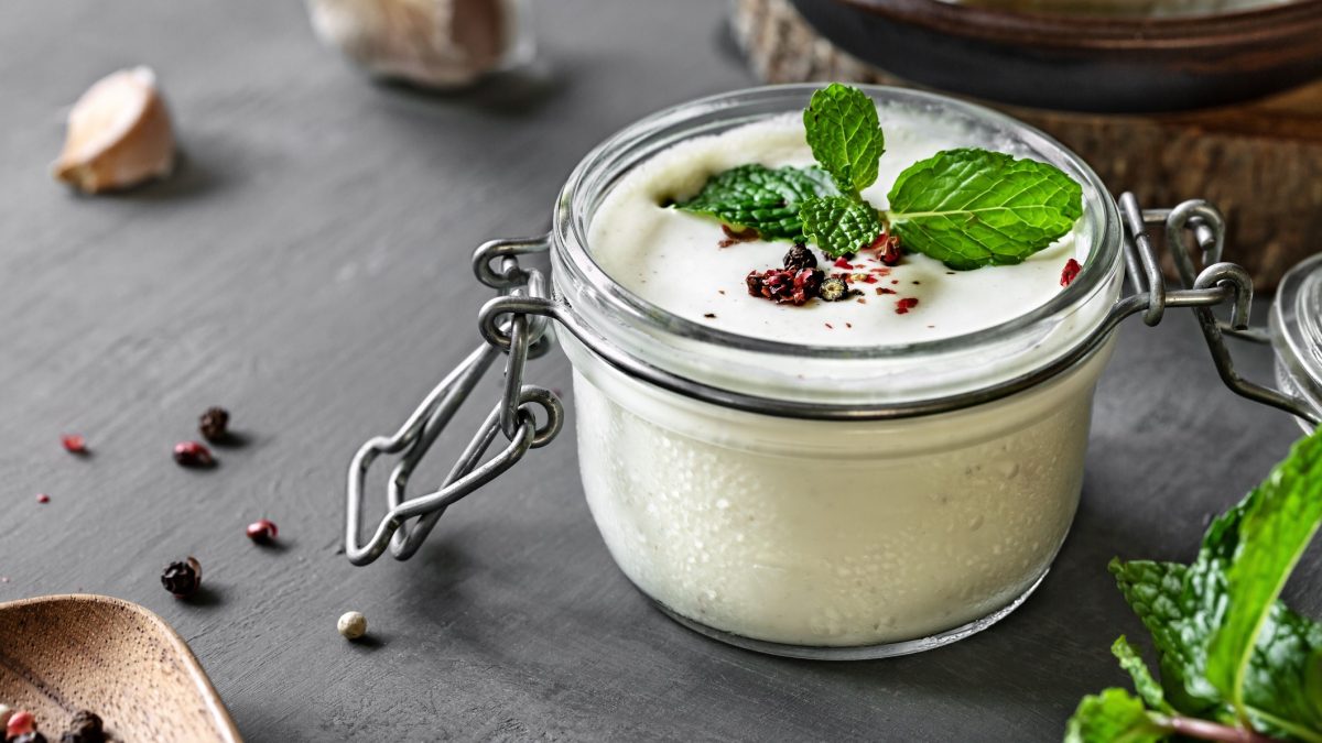 Feta-Zitronen-Dressing in einem Glas, dekoriert mit frischer Minze und Pfefferkörnern.