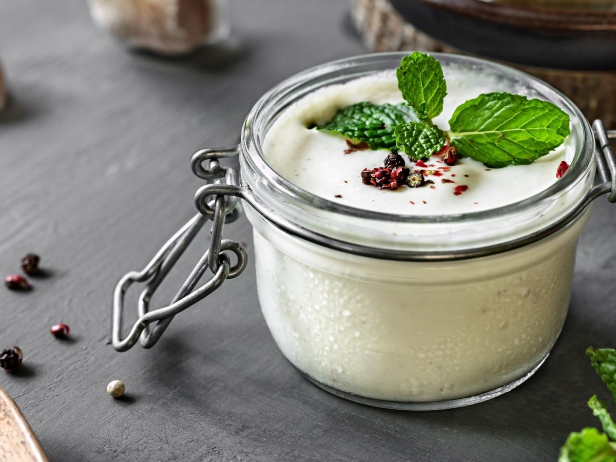 Feta-Zitronen-Dressing in einem Glas, dekoriert mit frischer Minze und Pfefferkörnern.