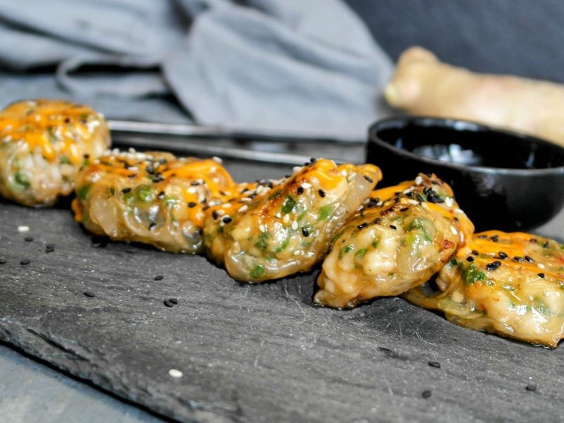 Das Fingerfood mit Garnelen auf einer schwarzen Schieferplatte und grauem Hintergrund. Alles von der Seite fotografiert.