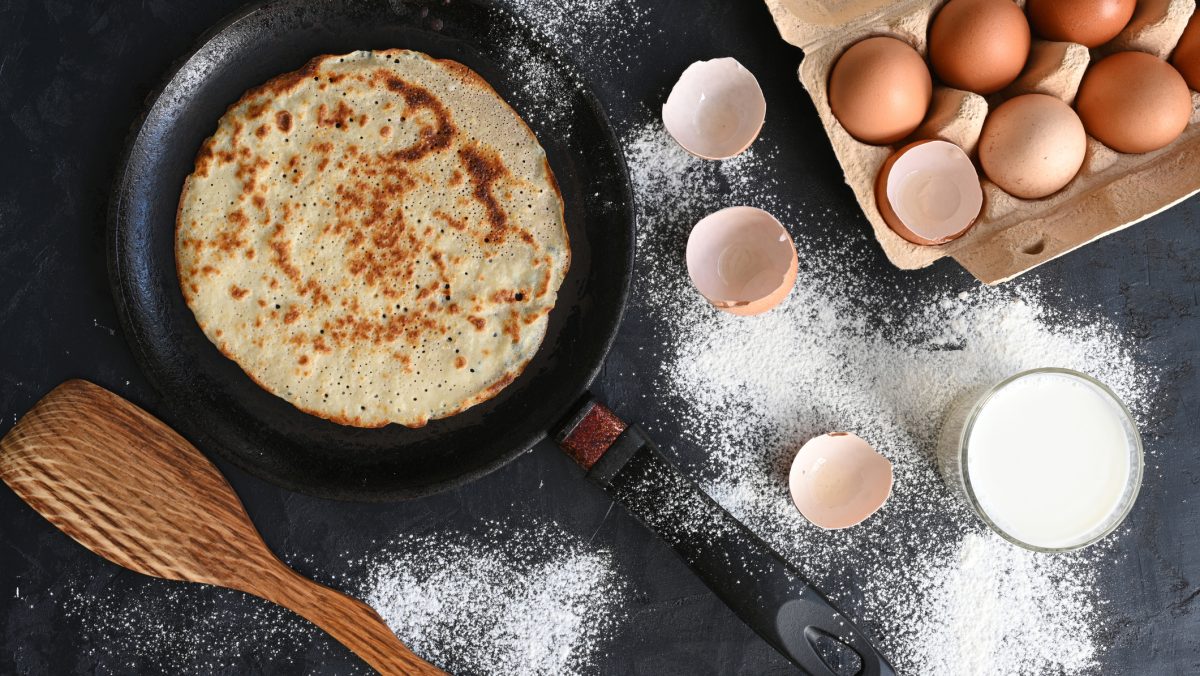 Draufsicht auf Pfannkuchen in Pfannkuchen, daneben Utensilien und Zutaten.