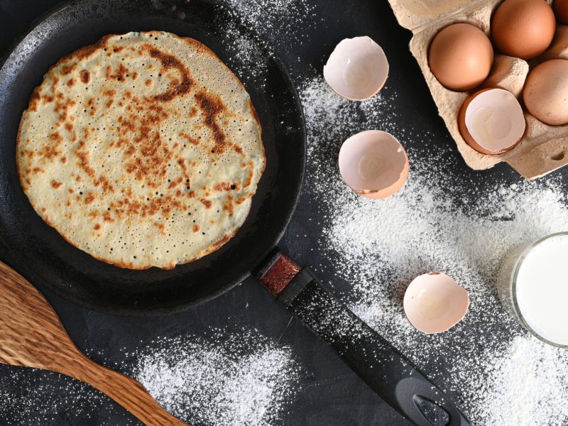 Draufsicht auf Pfannkuchen in Pfannkuchen, daneben Utensilien und Zutaten.