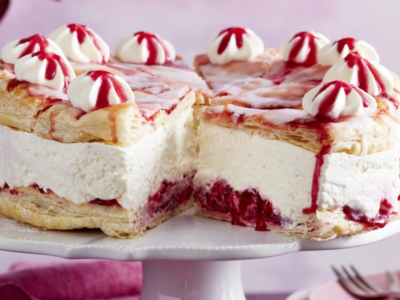 Holländer-Kirschtorte auf einem weißen Tortenteller auf rosa Hintergrund.