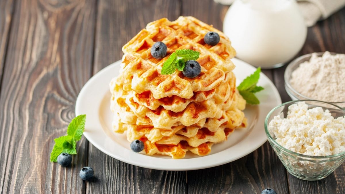 Mehrere Waffeln auf einem weißen Teller mit Blaubeeren und Minze auf einem rustikalen Holztisch.