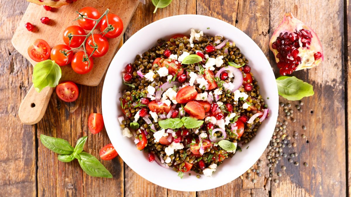 Linsensalat mit Feta von oben fotografier, daneben frische Tomaten und Basilikumblätter.