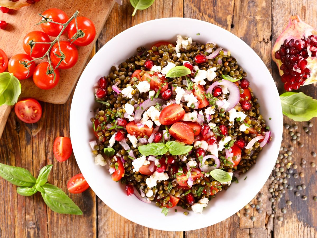 Linsensalat mit Feta von oben fotografier, daneben frische Tomaten und Basilikumblätter.